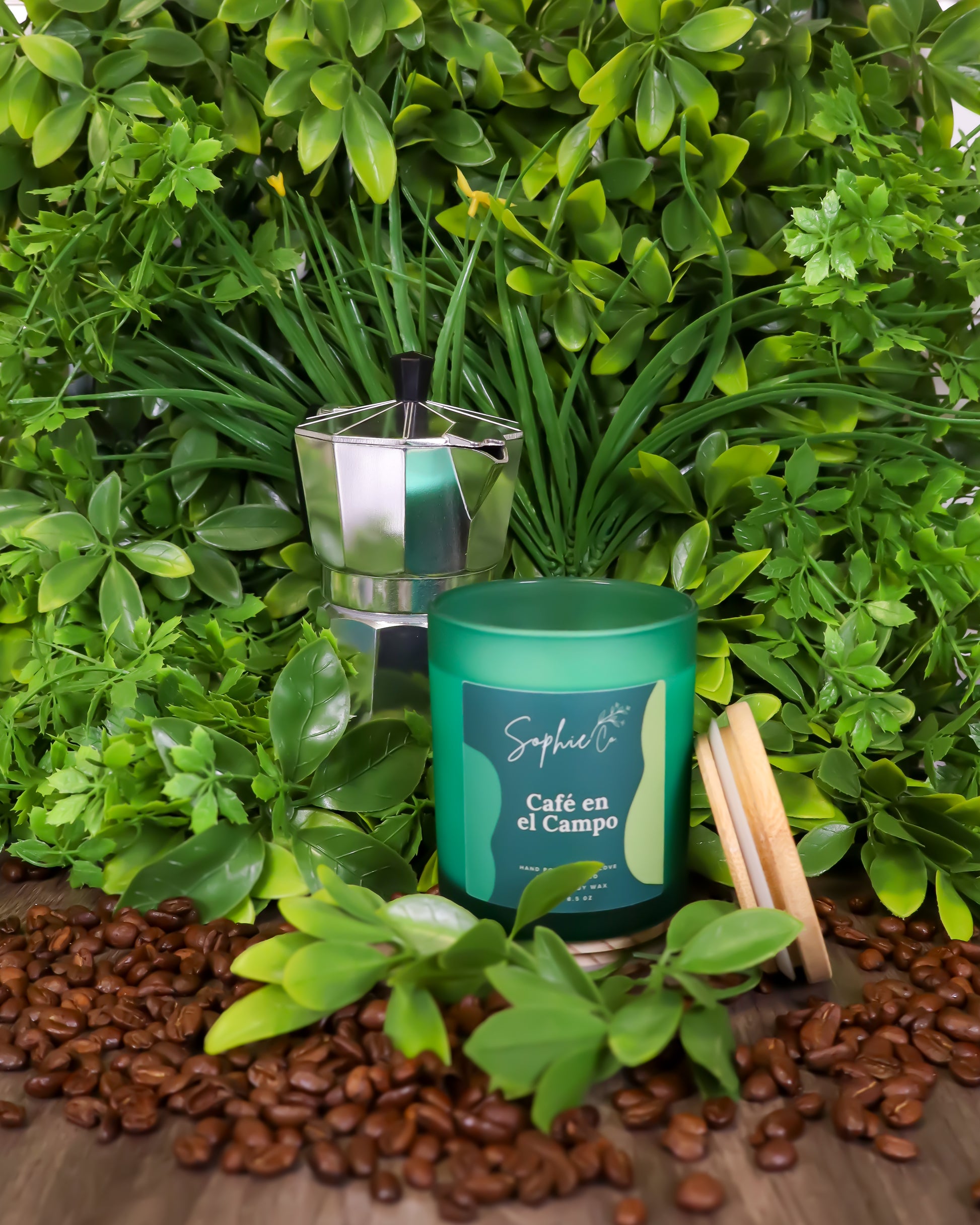 Hand poured soy wax candle labeled 'Café en el Campo' by Sophie Co on a wooden surface with coffee beans and greenery.