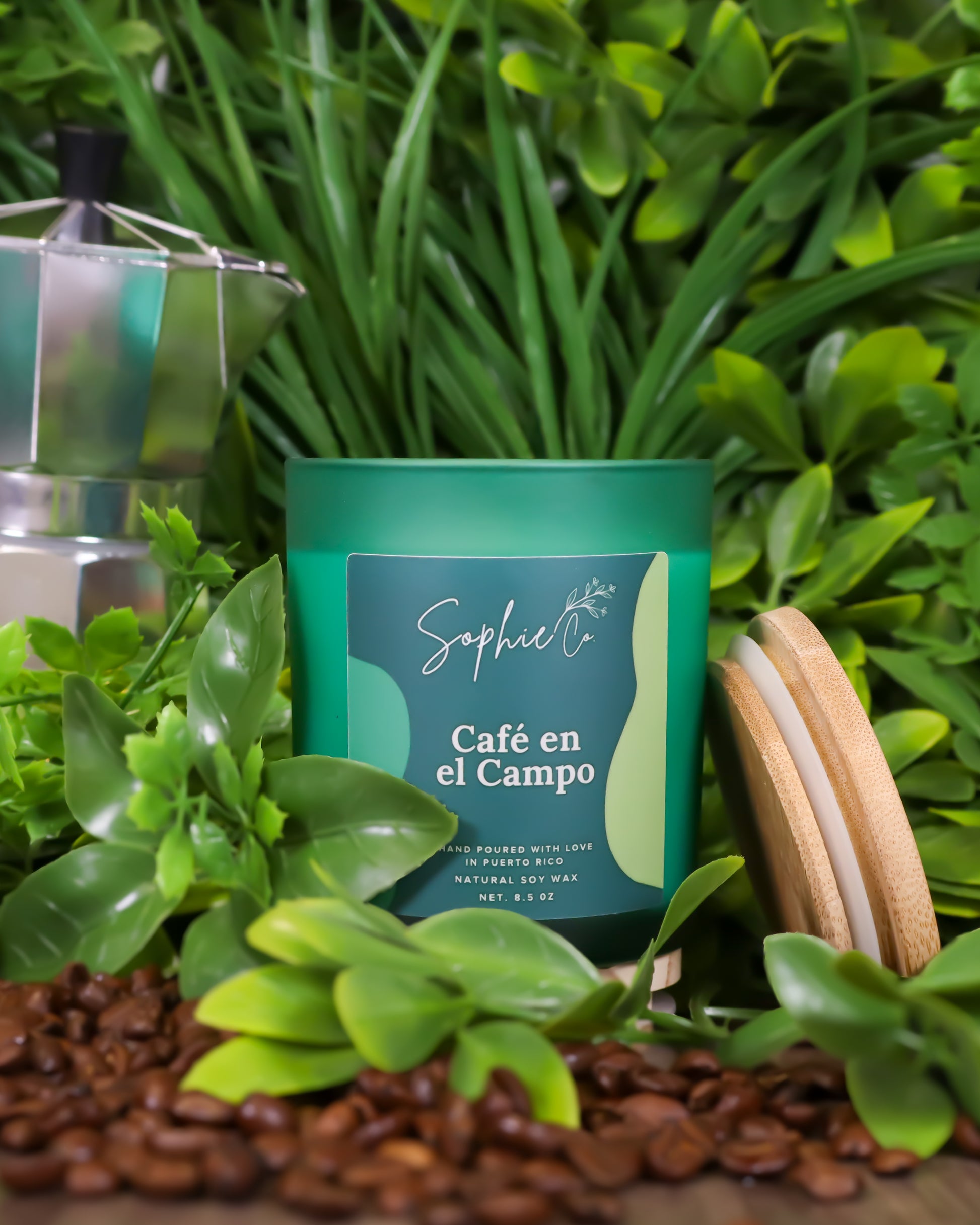 Hand poured soy wax candle labeled 'Café en el Campo' by Sophie Co on a wooden surface with coffee beans and greenery.
