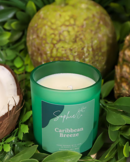Hand poured soy wax candle labeled 'Caribbean Breeze' by Sophie's on a green leafy background
