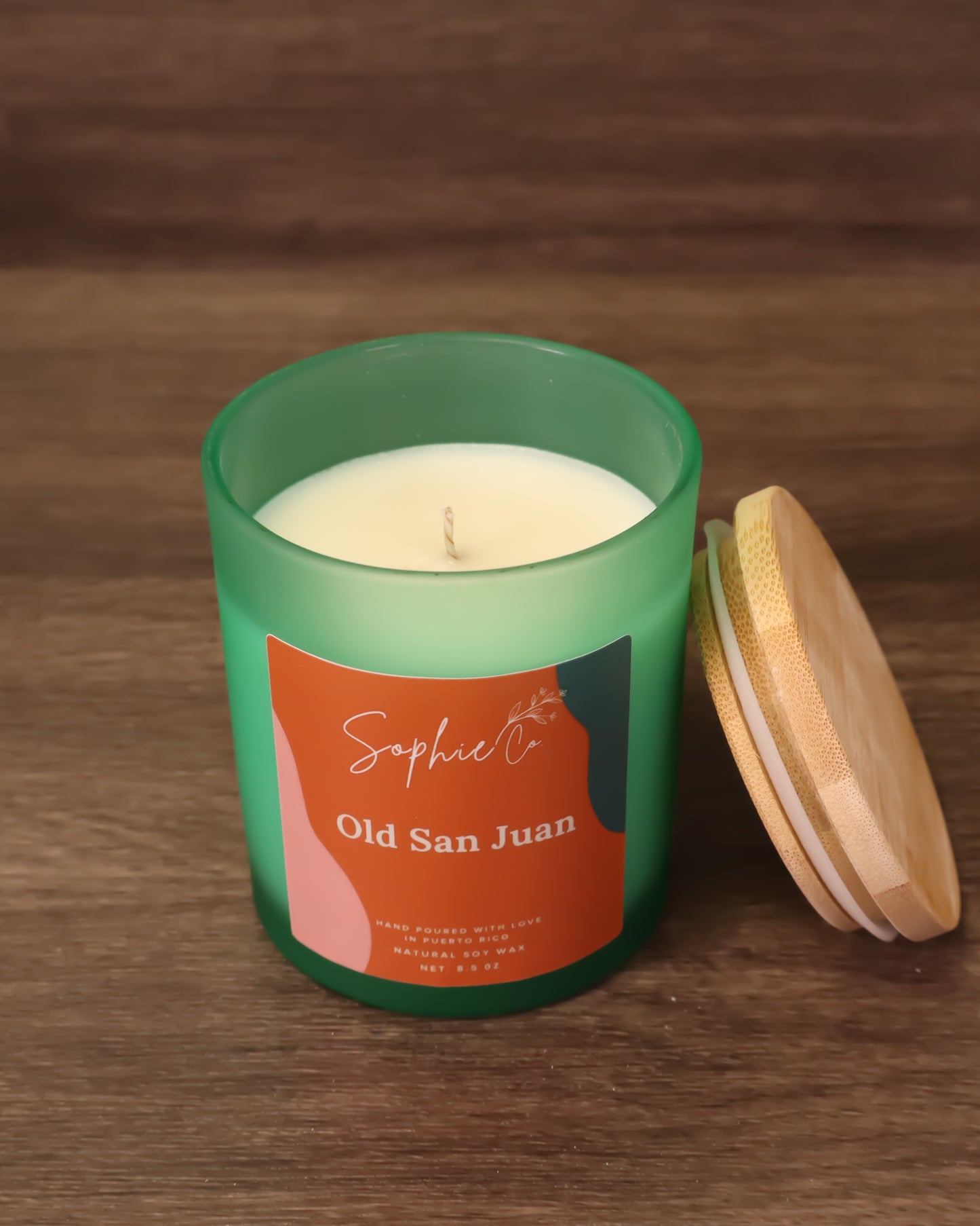 Hand poured soy wax candle with orange label featuring 'Sophie Co' and 'Old San Juan' on a blurred background.