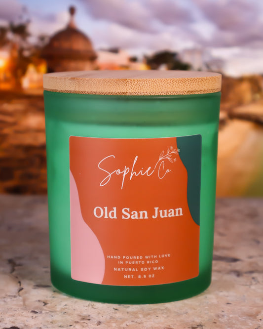 Hand poured soy wax candle with orange label featuring 'Sophie Co' and 'Old San Juan' on a blurred background.