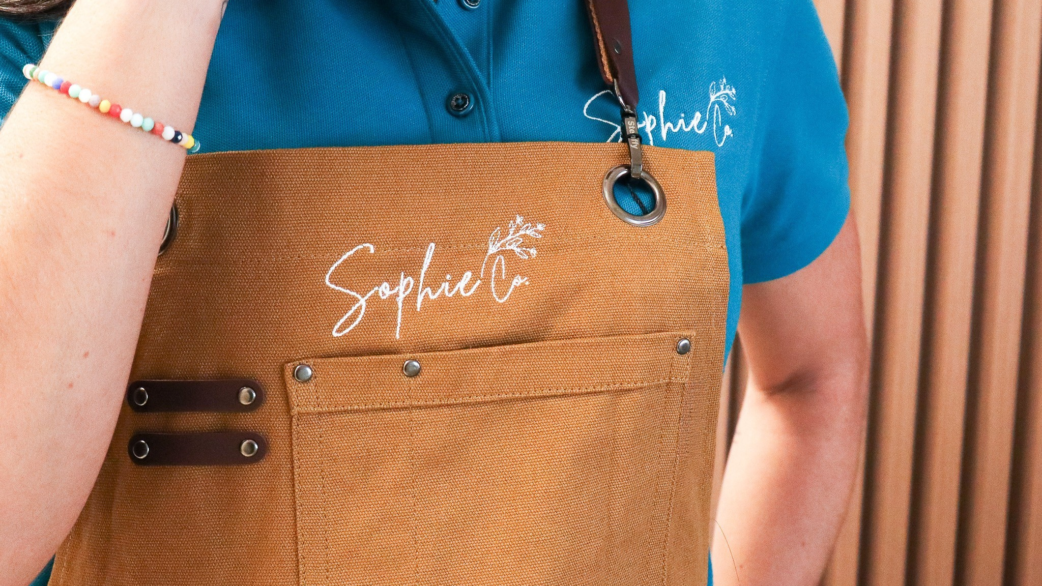 Person wearing a brown apron with 'Sophie Co' branding, standing against a neutral background.
